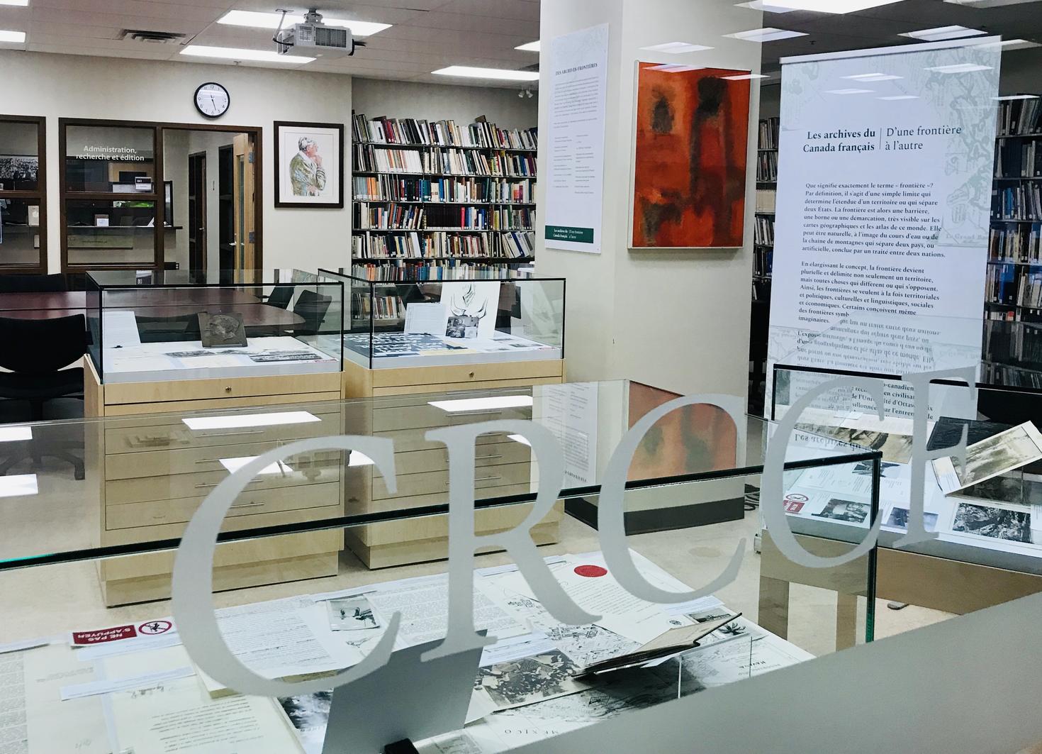 Vue d'une exposition dans une salle du CRCCF, avec des vitrines contenant des documents et artefacts, une affiche explicative sur chevalet, et des rayonnages d’archives en arrière-plan.