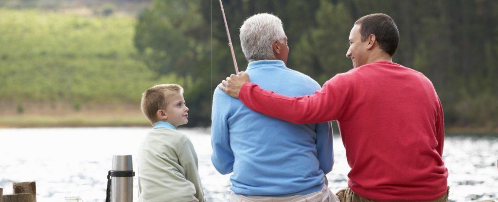 Père, fils et petit-fils assis sur un quai en train de pêcher.
