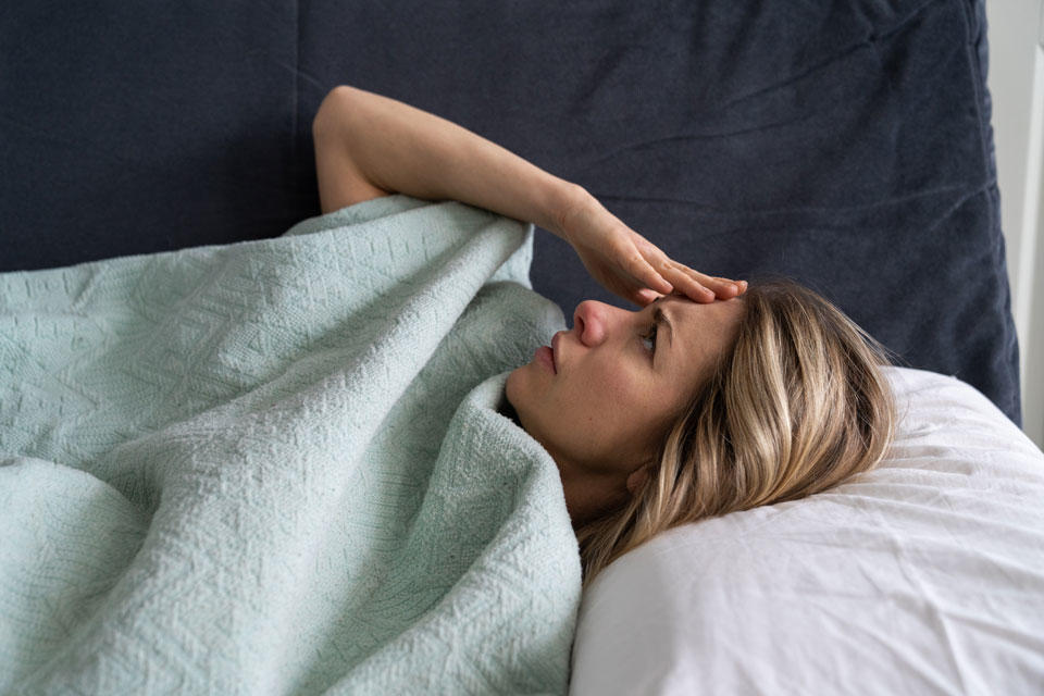 Femme au lit avec une main sur le front et des maux de tête