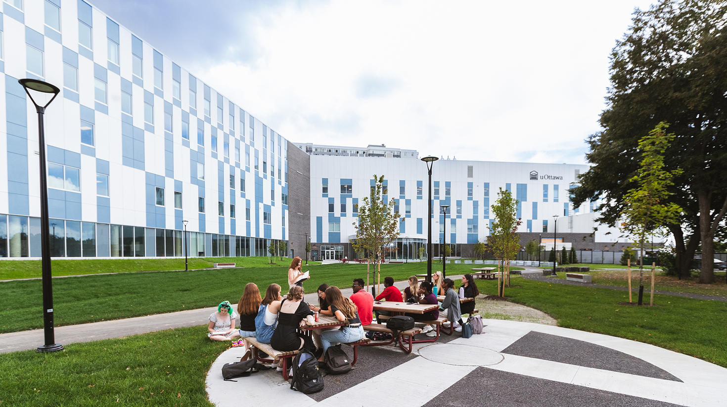 Étudiants assis sur des bancs de pique-nique à l'extérieur du bâtiment de la faculté des sciences de la santé.