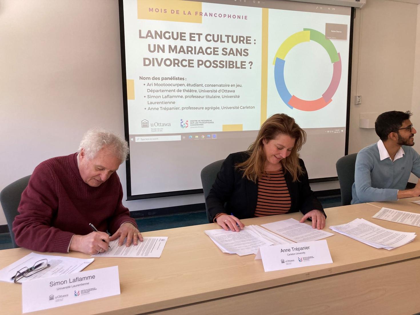 Trois des panélistes de la table ronde, assis et lisant des papiers.