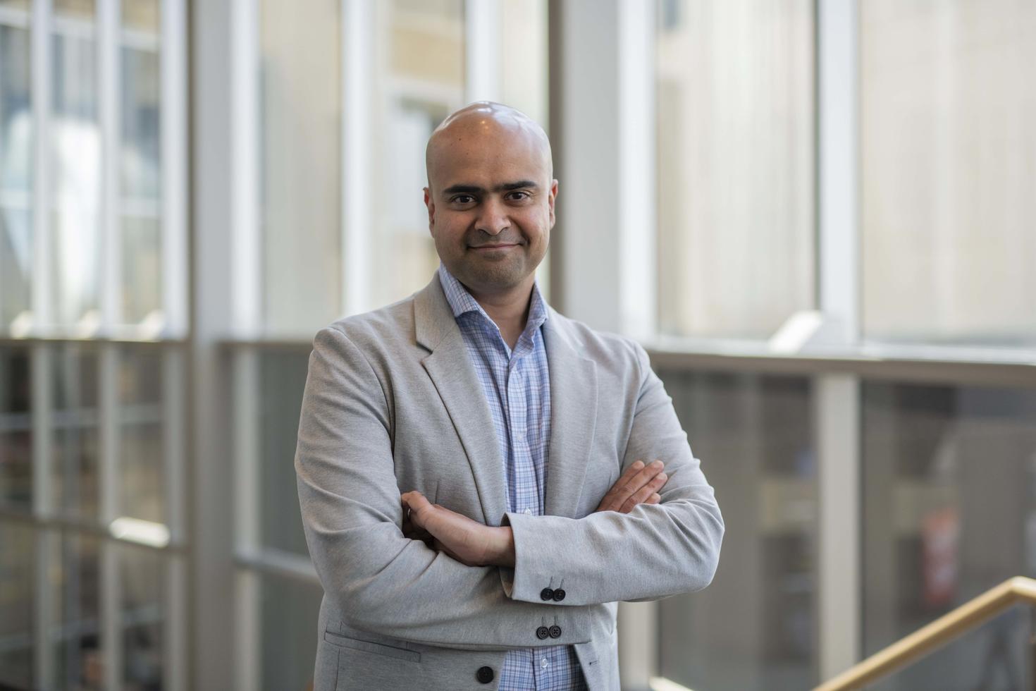 Harish Veeramani headshot by glass windows.