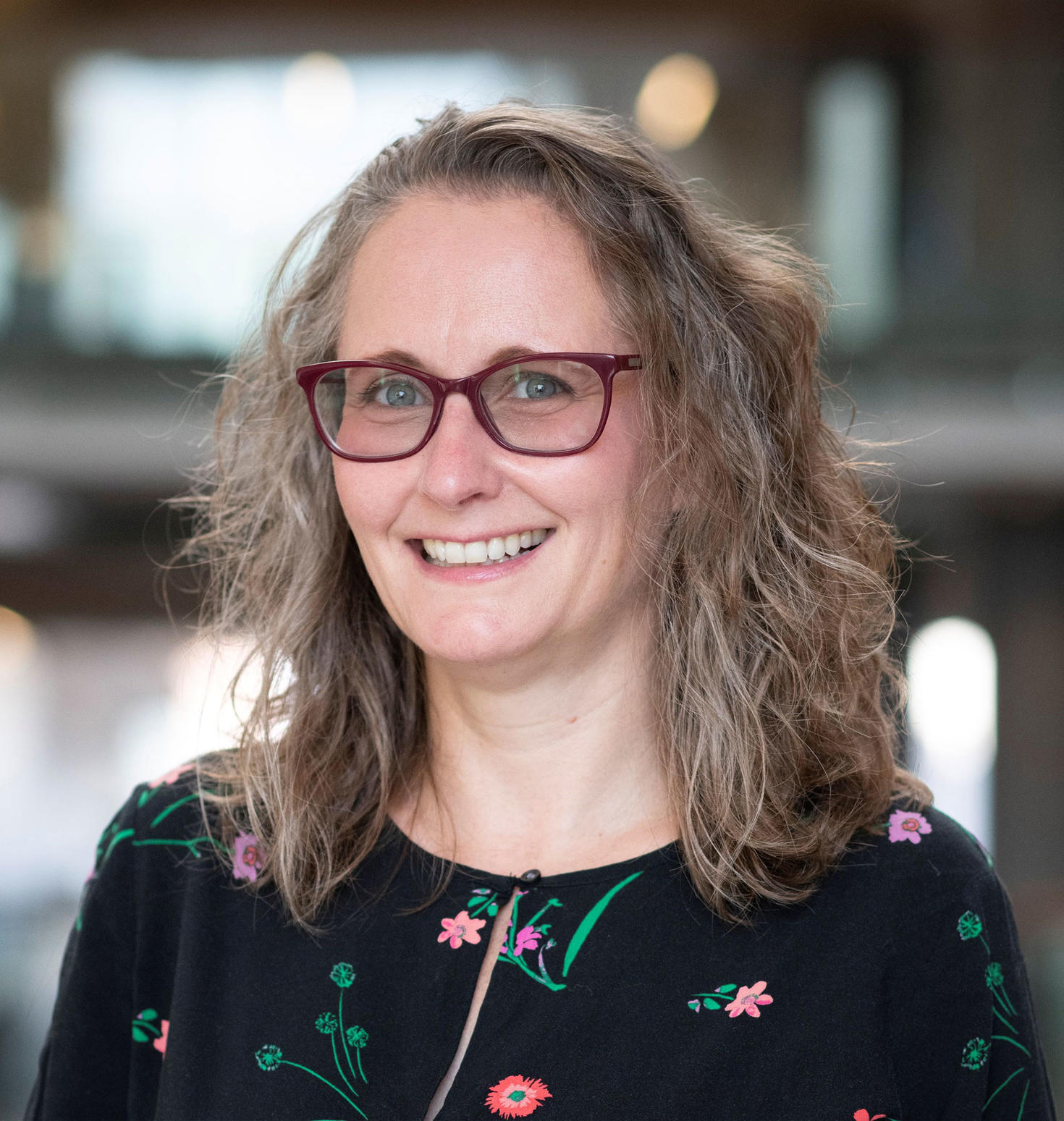 Portrait de la professeure Shanna Kousaie souriante, portant des lunettes et un haut à motifs floraux, avec un arrière-plan intérieur flou.