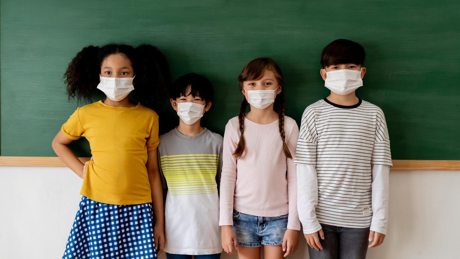 Jeunes étudiants portant des masques devant un tableau scolaire.