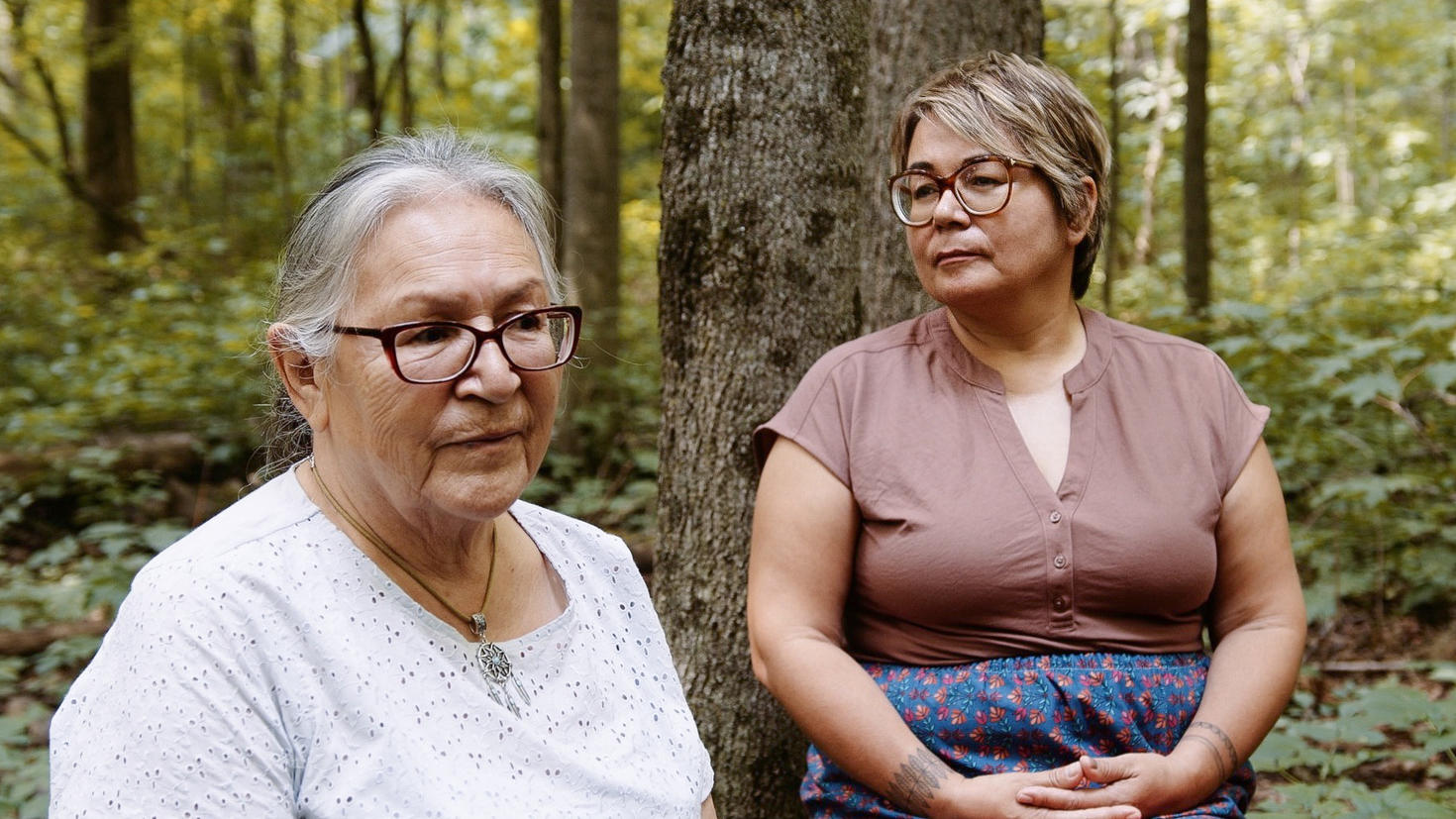 Mariette Niquay and Eva Ottawa sitting on a log in the woods