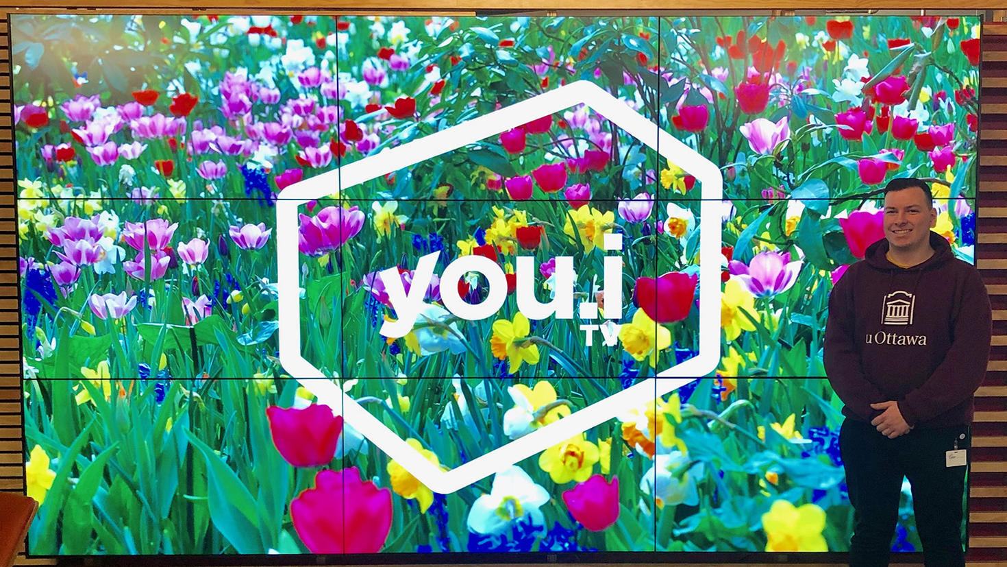 A young man stands in front of a big screen showing a lot of flowers.