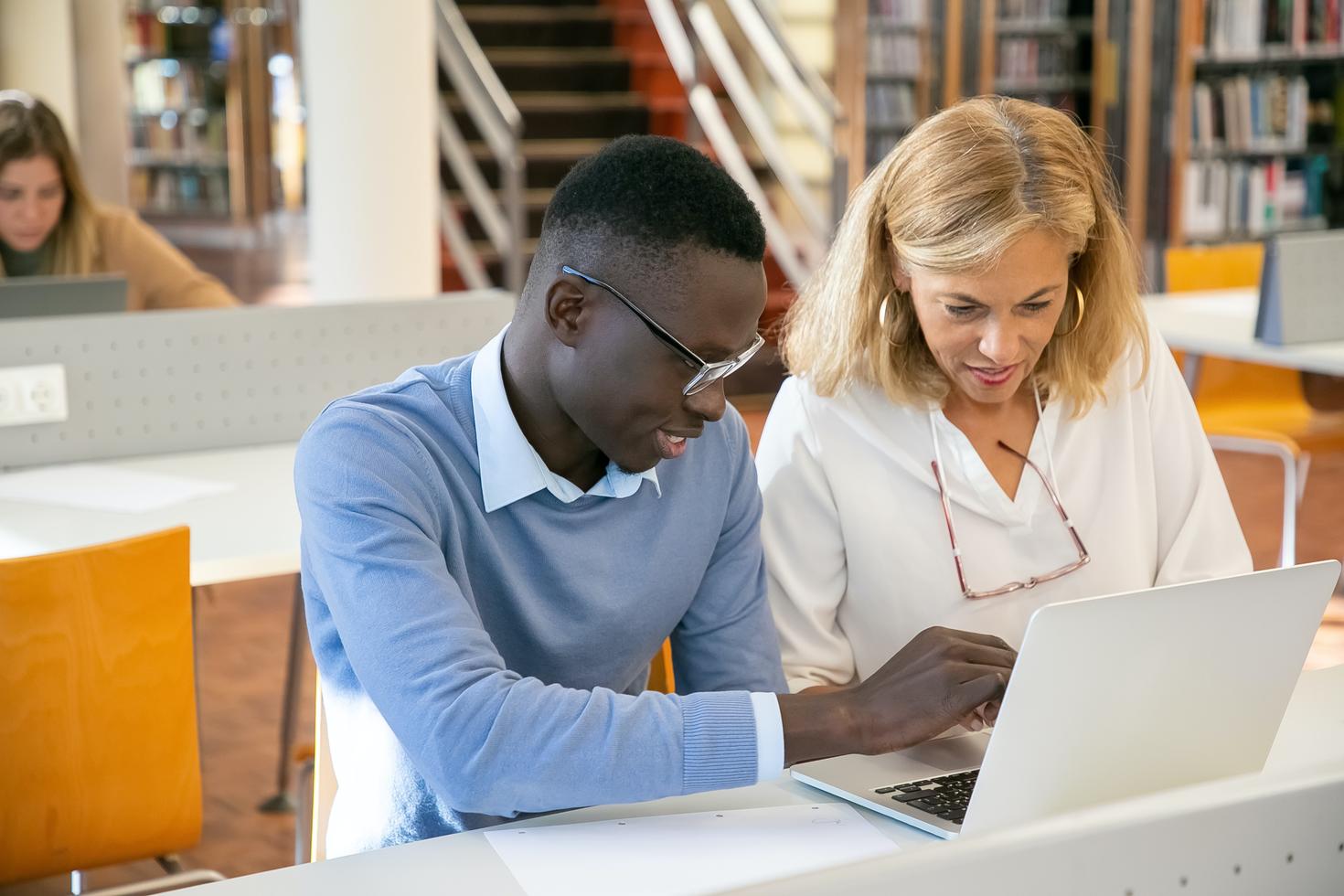 Teacher helping student working on laptop in library