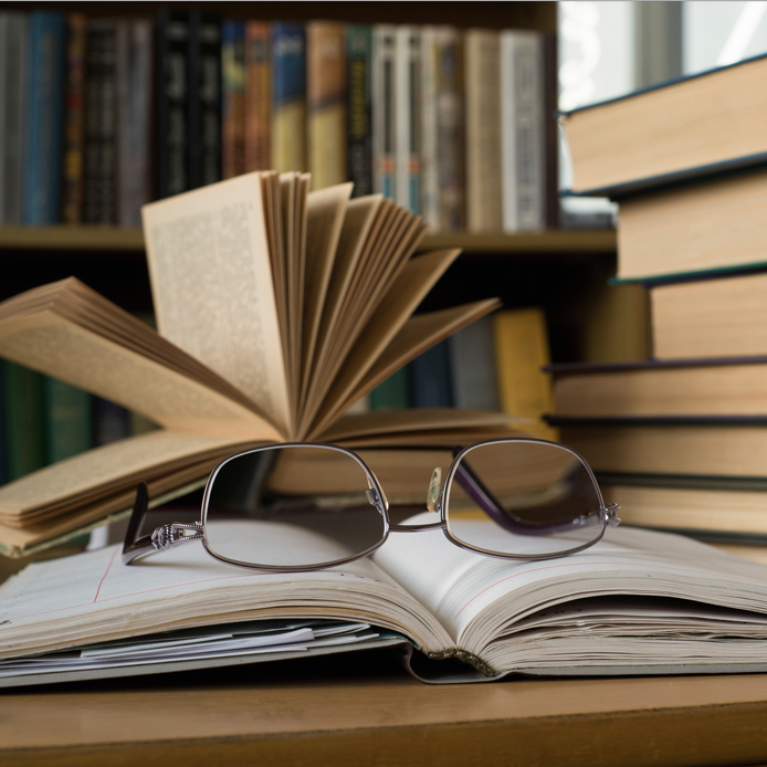 Book stack on the side, and eyeglass on an open book in the center.