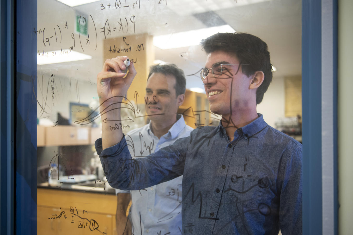 Two researchers writing formulas and research on glass. 