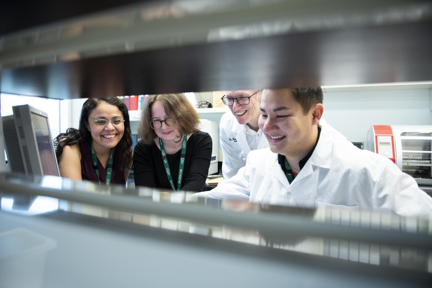 Researchers in lab all looking at something hidden and smiling.