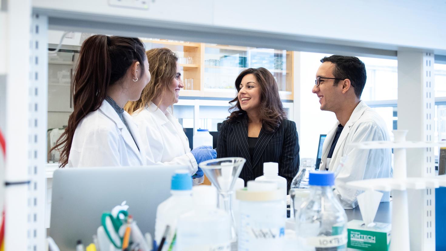 Four researchers, including Dr. Nafissa Ismail, are talking and smiling in a lab.