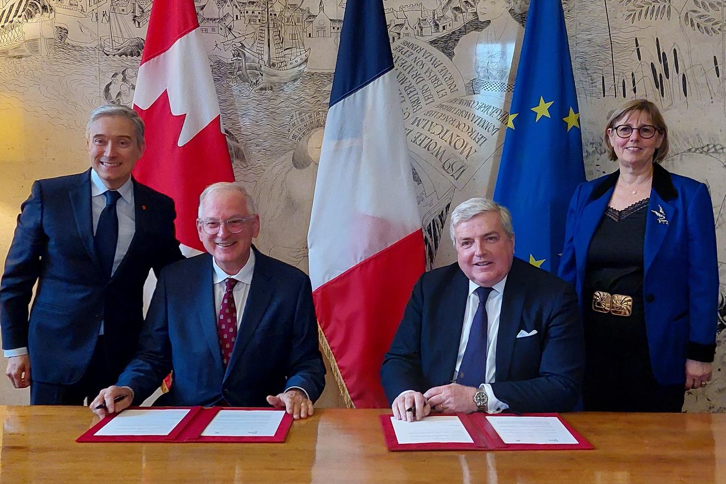 Four people are standing and sitting in front of flags
