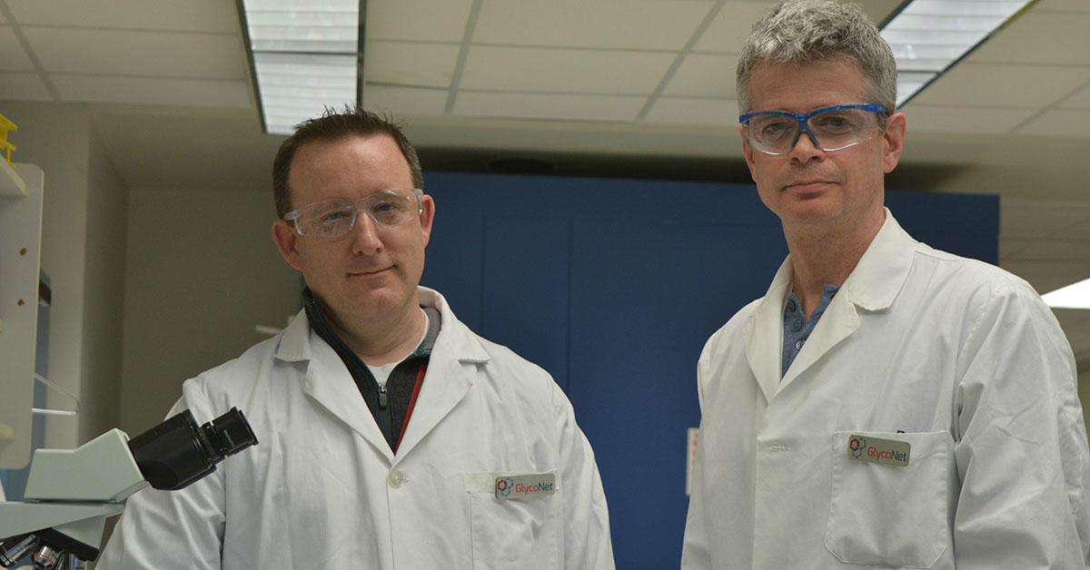 Researchers Jason Acker and Robert Ben posing in lab coats and protective glasses