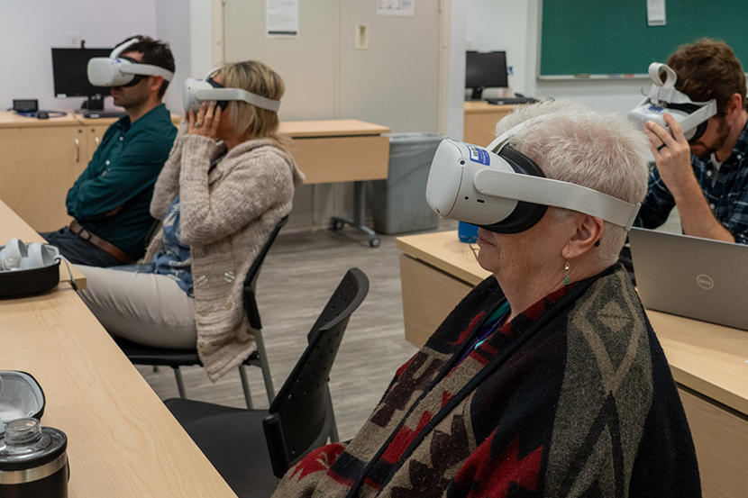 People sit at tables viewing a film through a virtual reality headset.