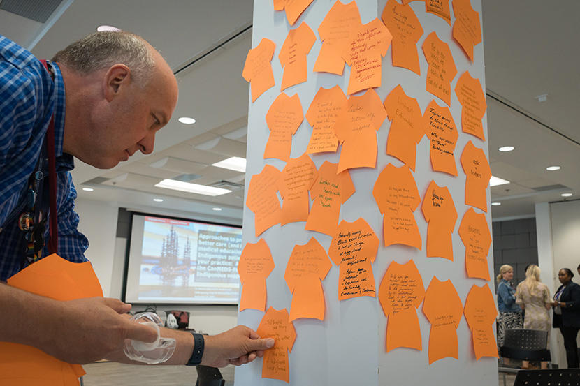 Dr. Eric Wooltorton adds a piece of orange paper in the shape of T-shirt to a wall.