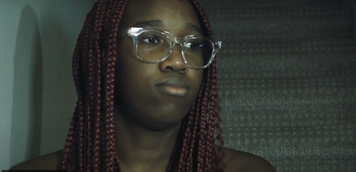 A person with long braids and glasses looking to the side