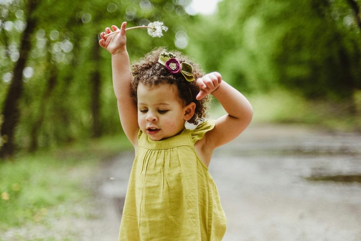 Child in yellow dress holding shedding dandelion