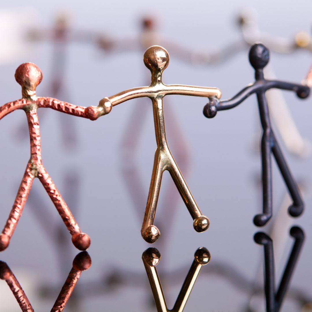 Sculpture of stick figures made of different metals holding hands in a circle