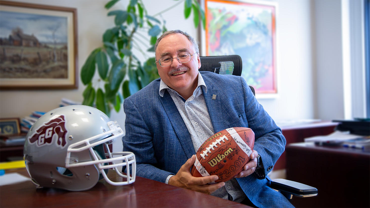 Sylvain Charbonneau in his office holding a football signed by the Gee-Gees team
