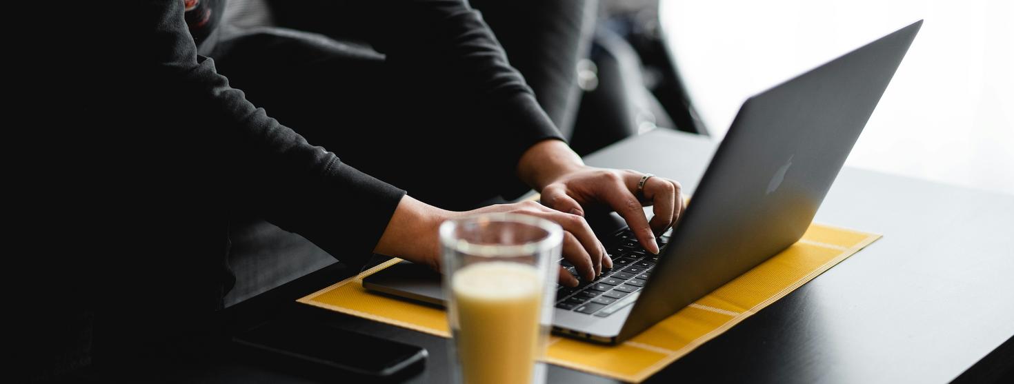 Person typing on a laptop at a table with a drink in the foreground