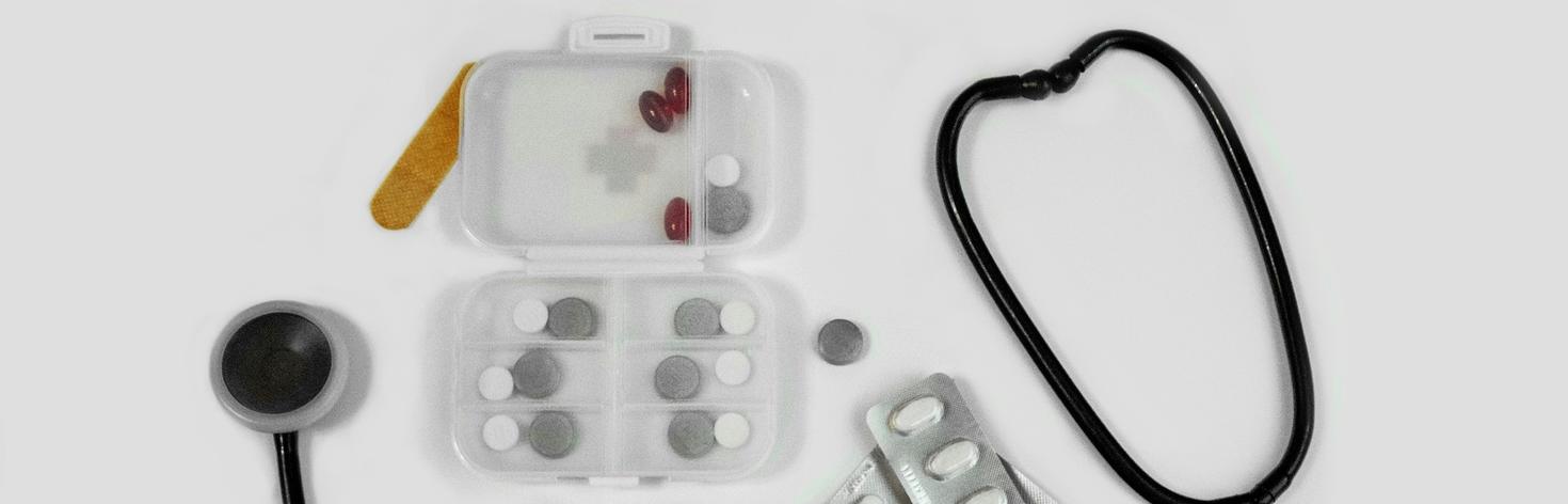 Small pill organizer, assorted pills, a bandage, and a stethoscope on a table