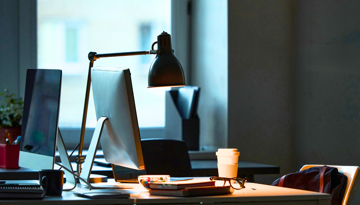 A desk with two screens and a lamp.