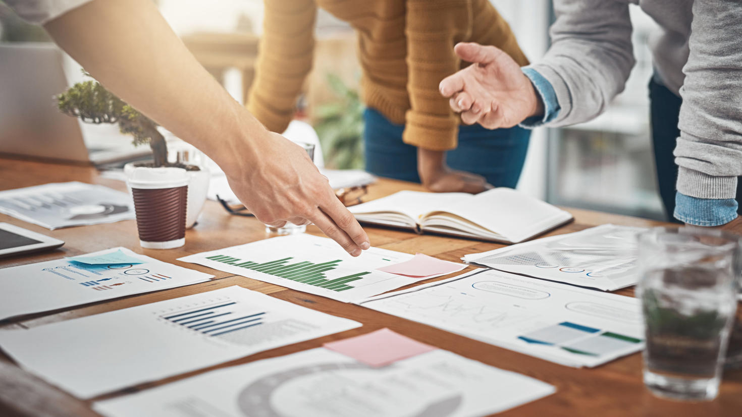 People collaborating at a table with charts, graphs, and documents spread out, pointing and discussing data.