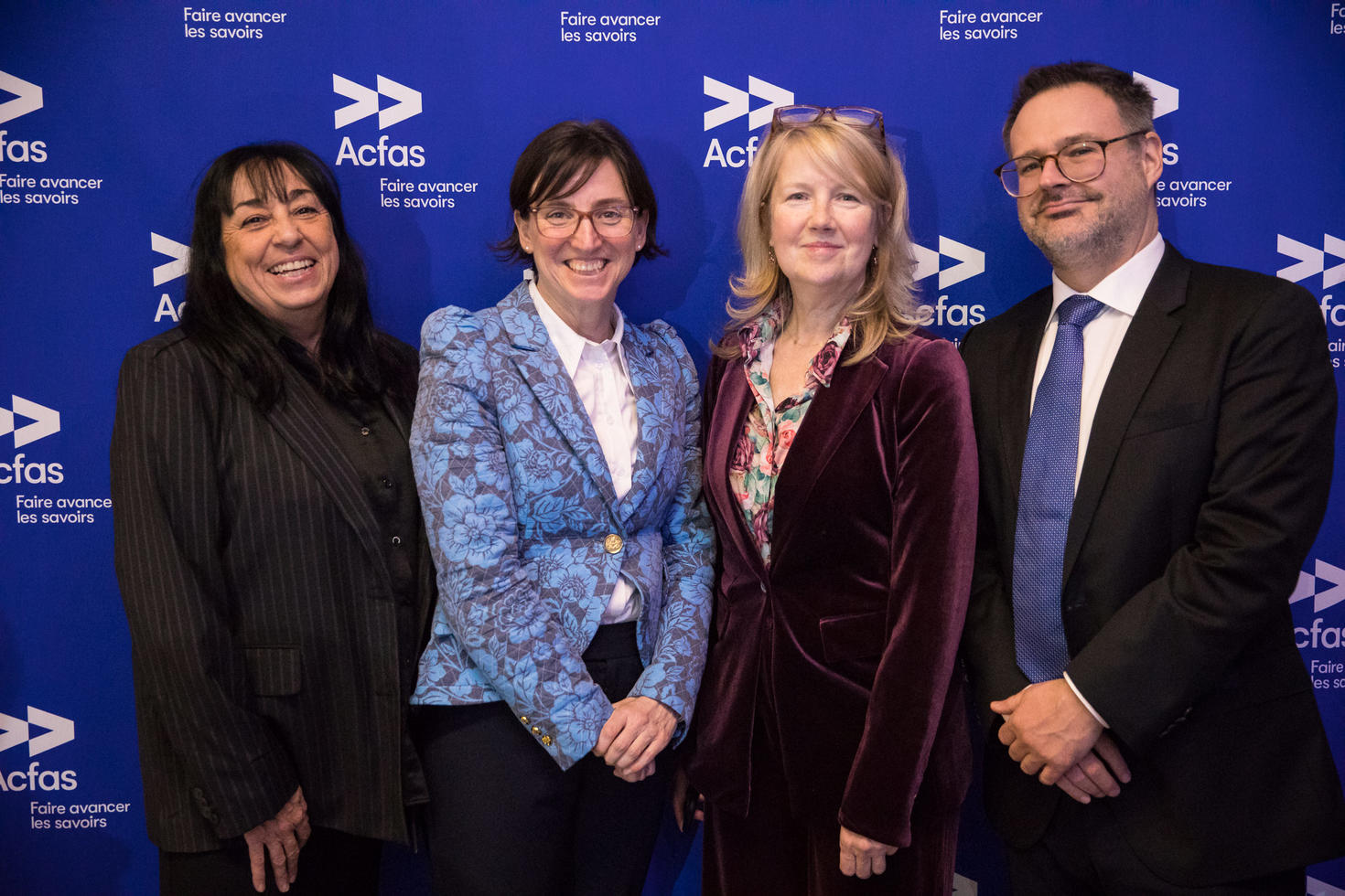 Four people standing in front of Acfas logo wall.