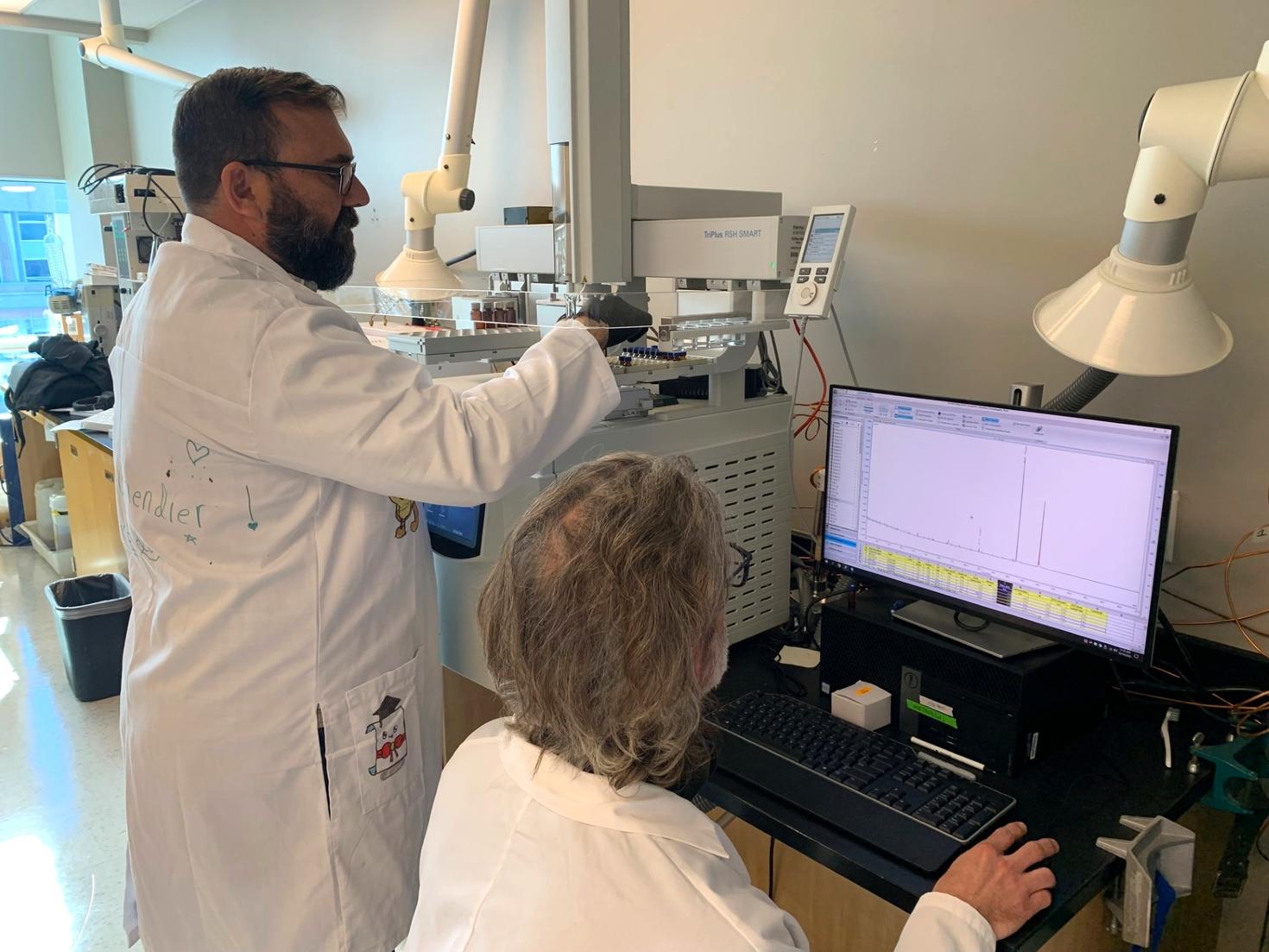 Professor Adam Shuhendler (standing) and Professor Cory Harris (seated) working together in a research laboratory.