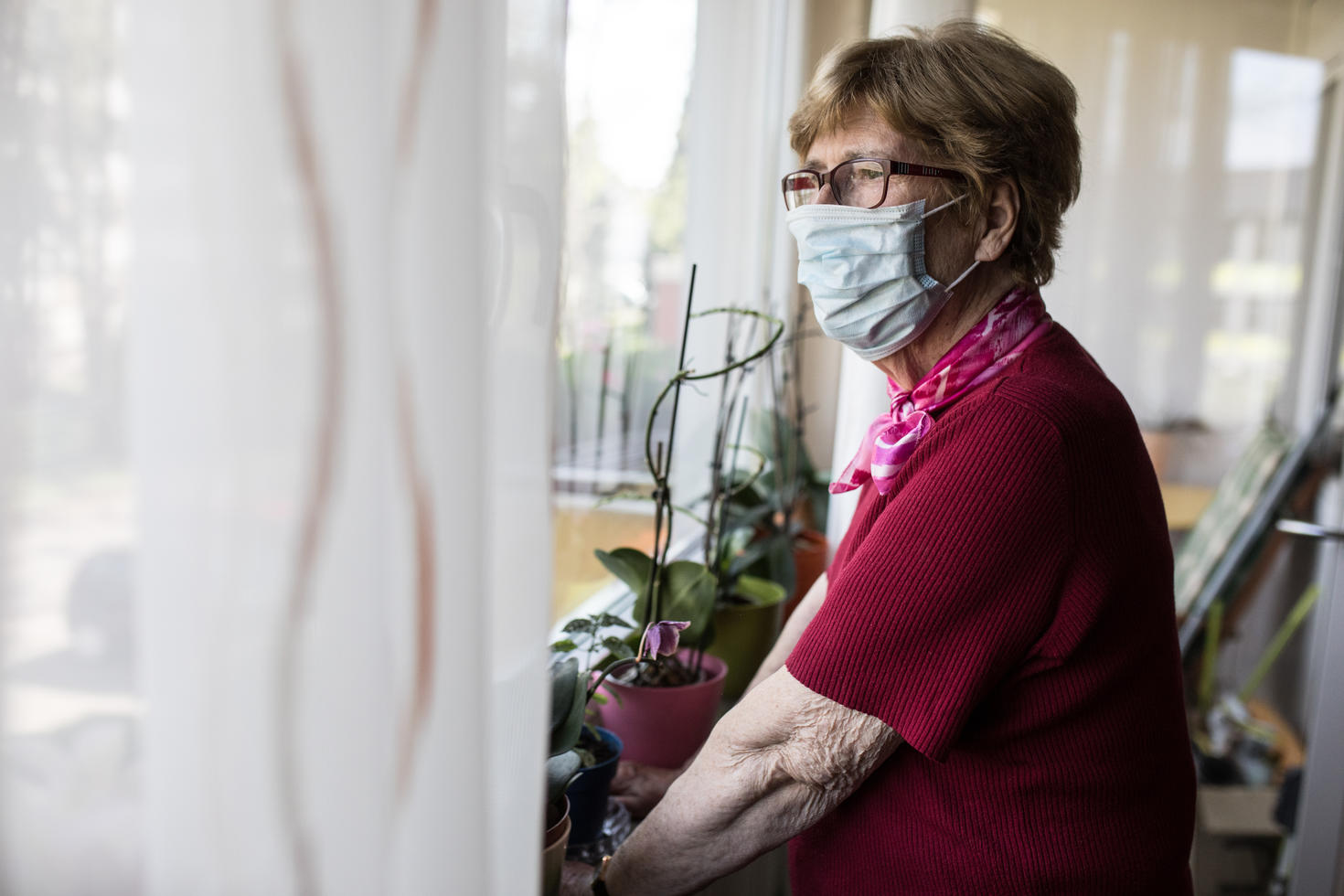 An elderly woman wearing a face mask looking out the window
