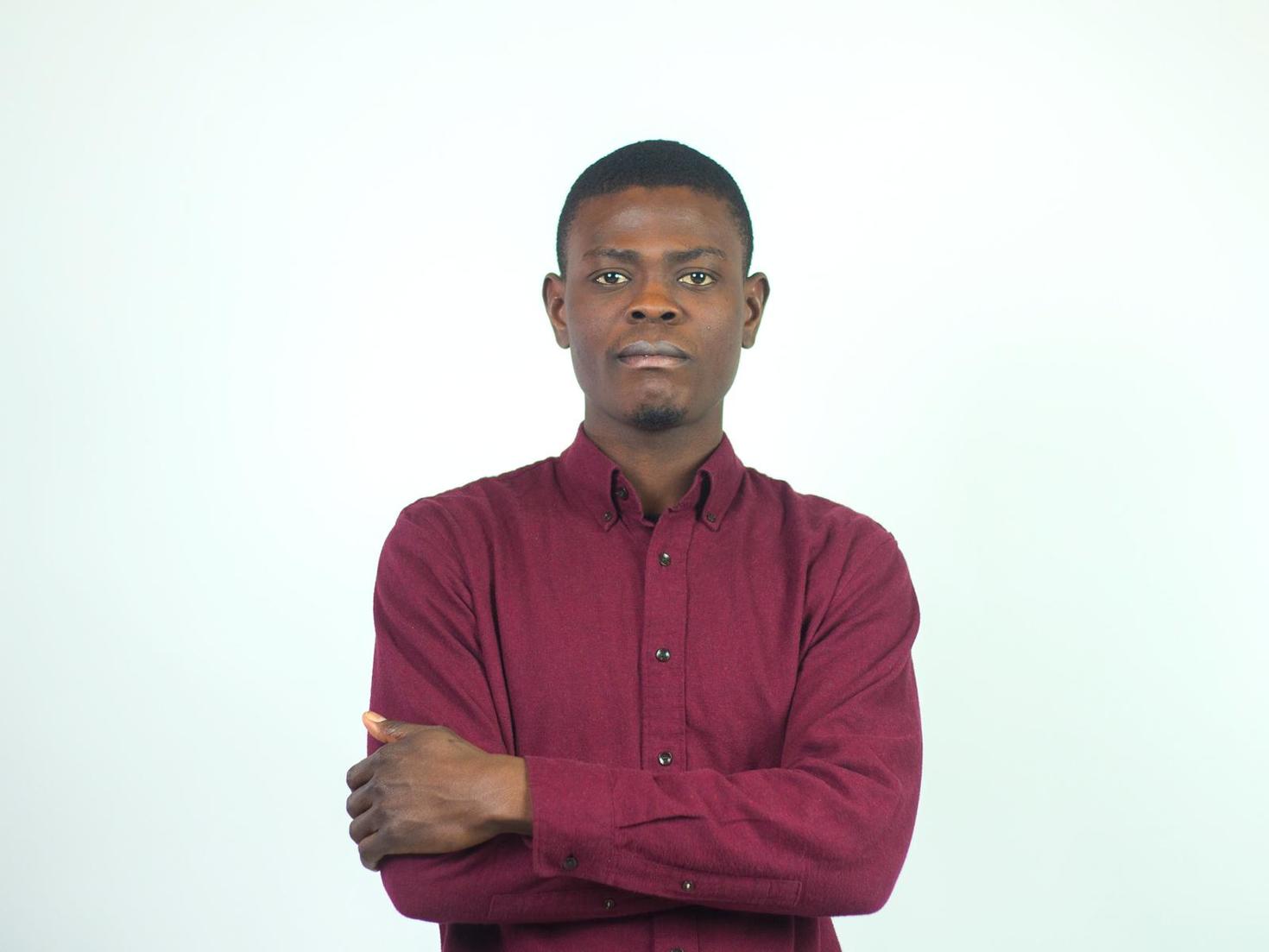 Portrait of Pierre Jameson Beaucejour, wearing a maroon button-down shirt, standing with his arms crossed. 