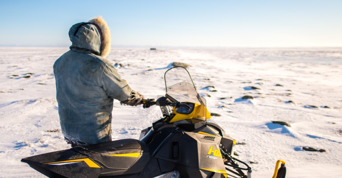 Un Inuit se tenant à côté de sa motoneige en Arctique Un Inuit se tenant à côté de sa motoneige en Arctique