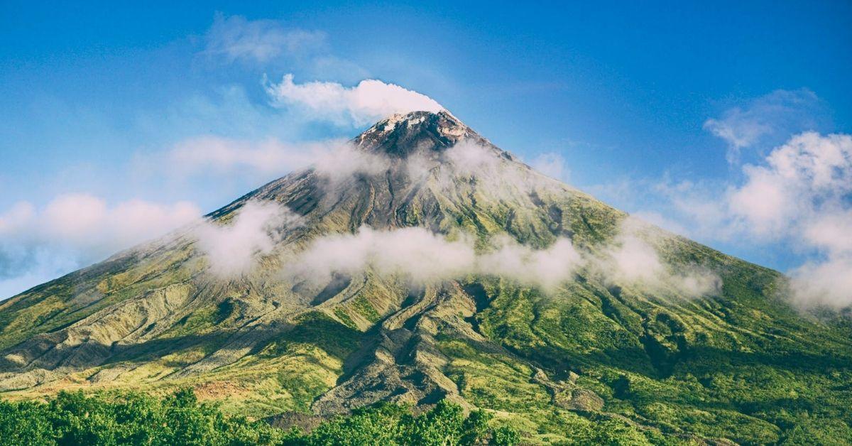 Une montagne couverte de verdure entourée de nuages