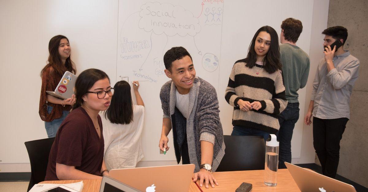 Des étudiants travaillent en classe, certains écrivent sur un tableau blanc.