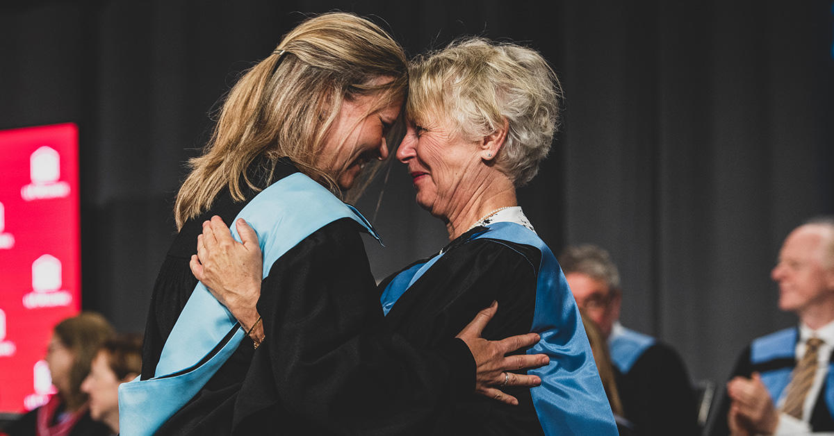 Two women wearing the graduation gown hug each other at graduation.