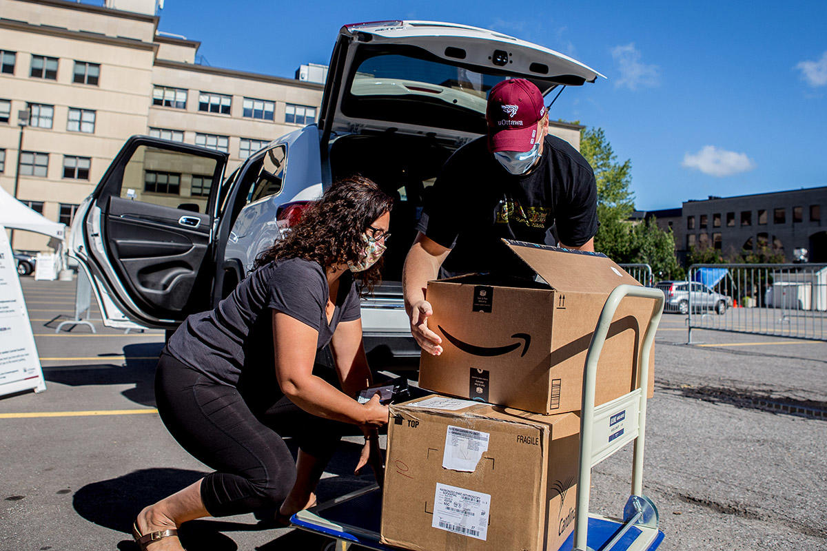 student lifts box on cart while mother helps him