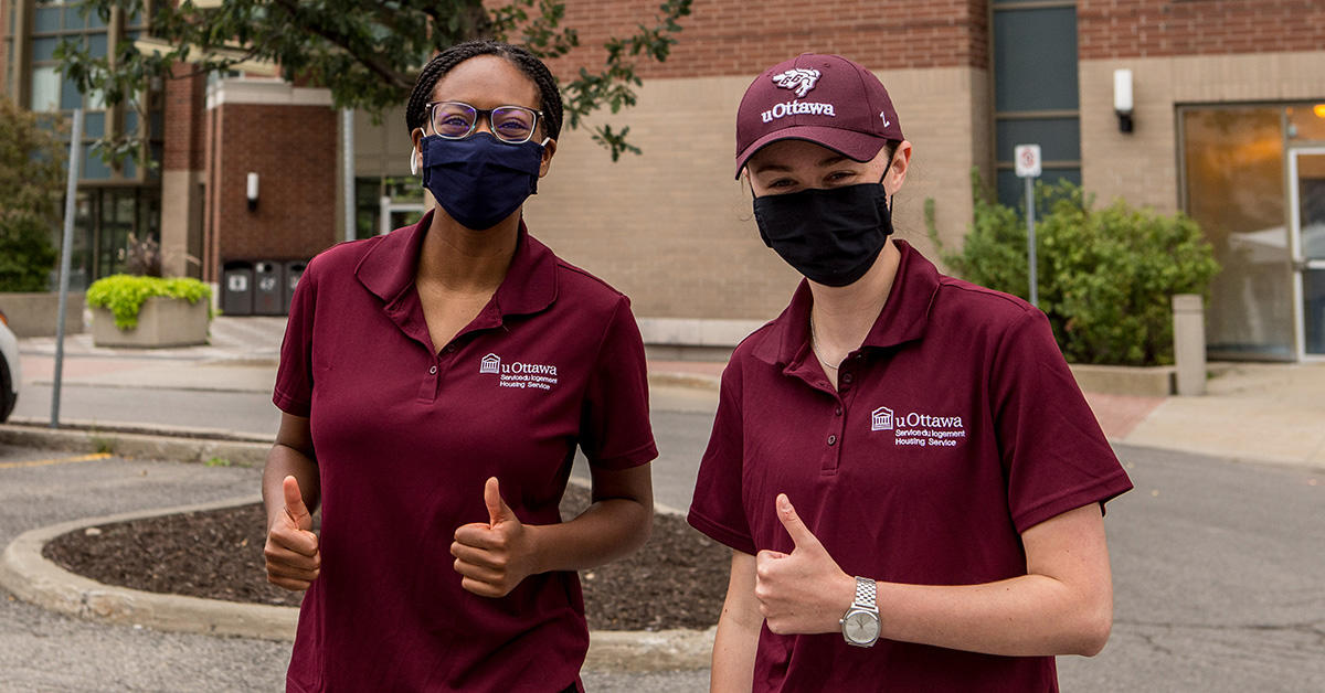 two students in housing services t-shirts wearing face masks and giving thumbs up