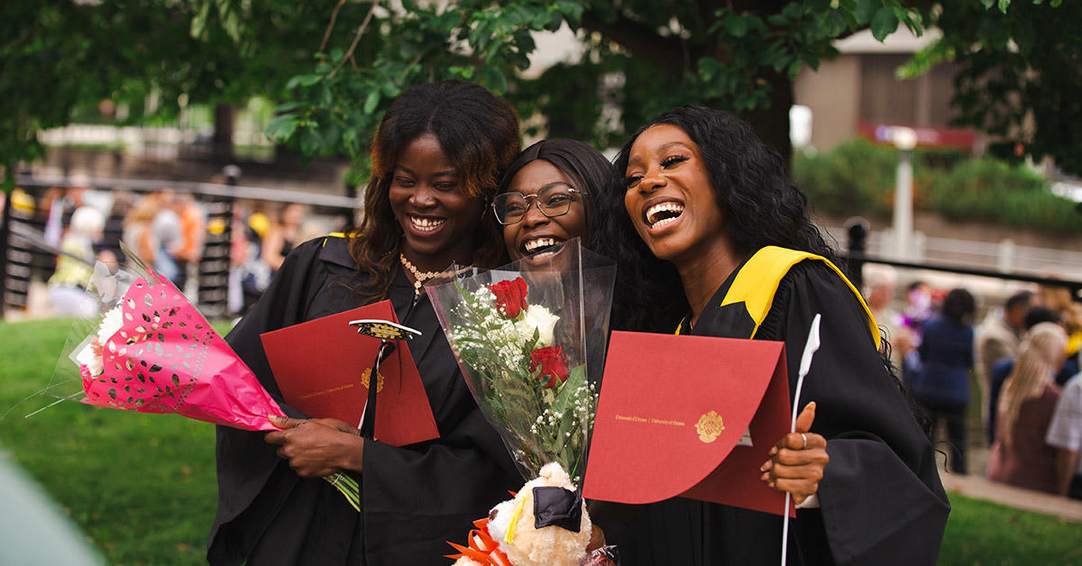 trois diplômés de la faculté des sciences sourient et rient en tenant leur diplôme. 