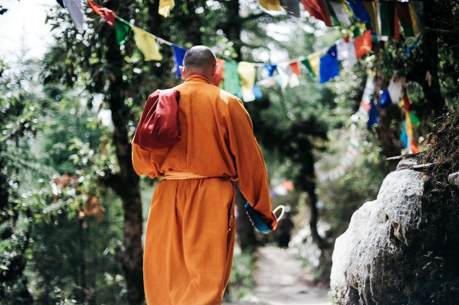Picture of a Nepalese walking in a forest while wearing an orange traditional outift. Threes and plants on both sides