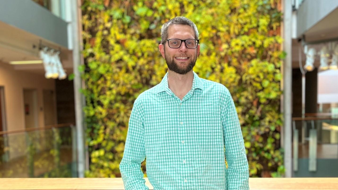  Le professeur Aaron Tikuisis, vêtu d'une chemise à carreaux vert menthe et blanc, se tient devant le mur vivant du bâtiment FSS sur le campus d'Ottawa