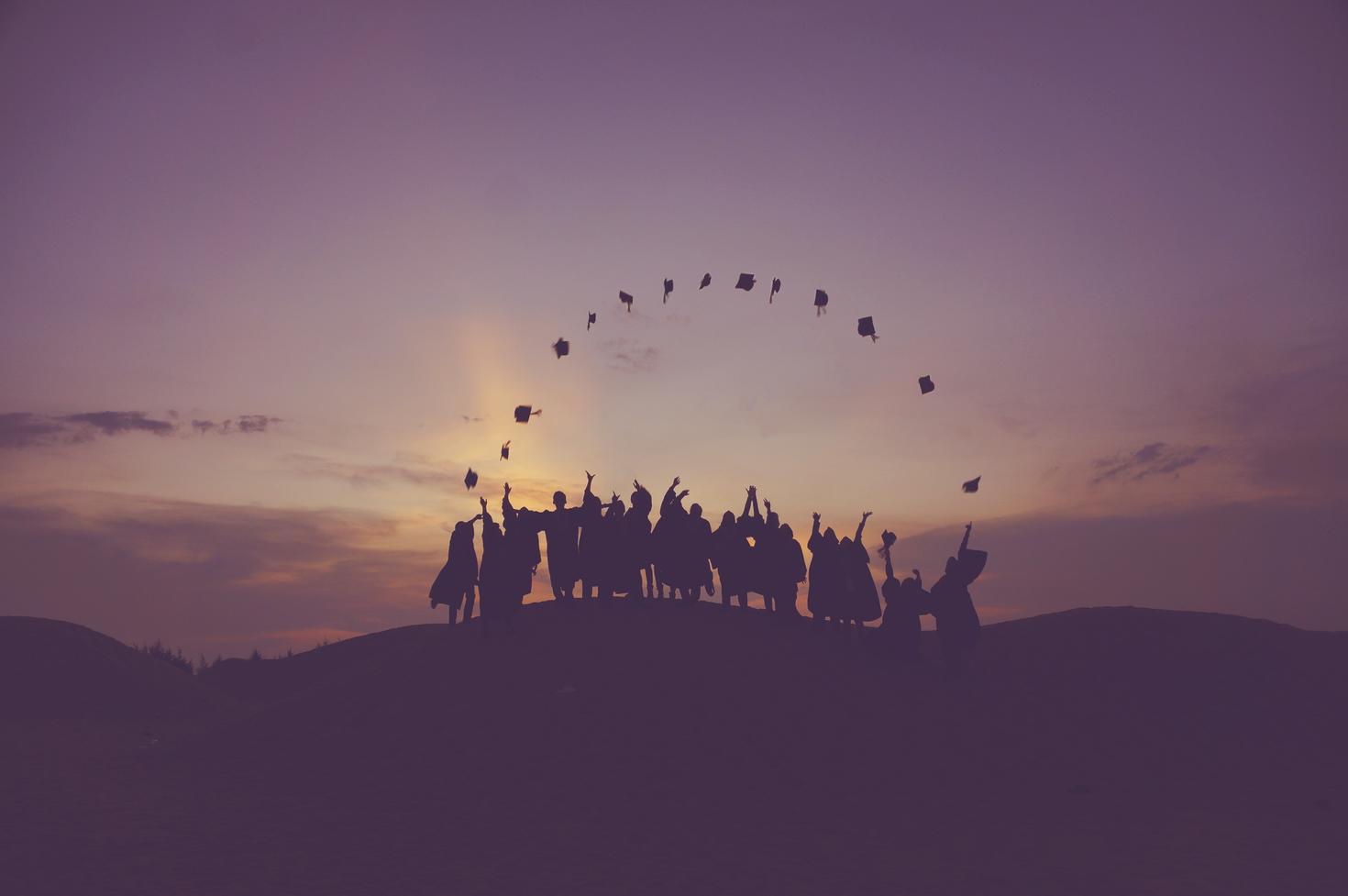 students celebrate by throwing their hats at sunset