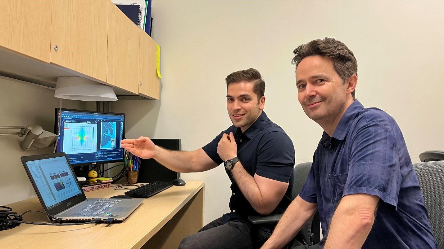 PhD student Parviz Ajourlou (left) sharing research results with Professor Glenn Milne (right). They are both seated at a desk in front of a laptop and a computer screen.