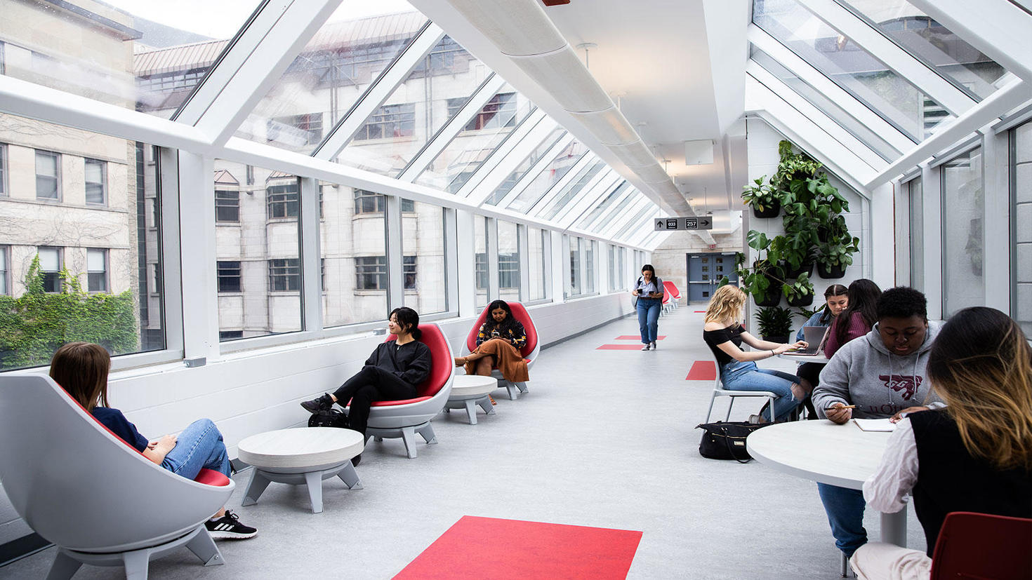 Couloir rempli de fenêtres sur le campus avec des étudiants travaillant sur des bureaux et des chaises.
