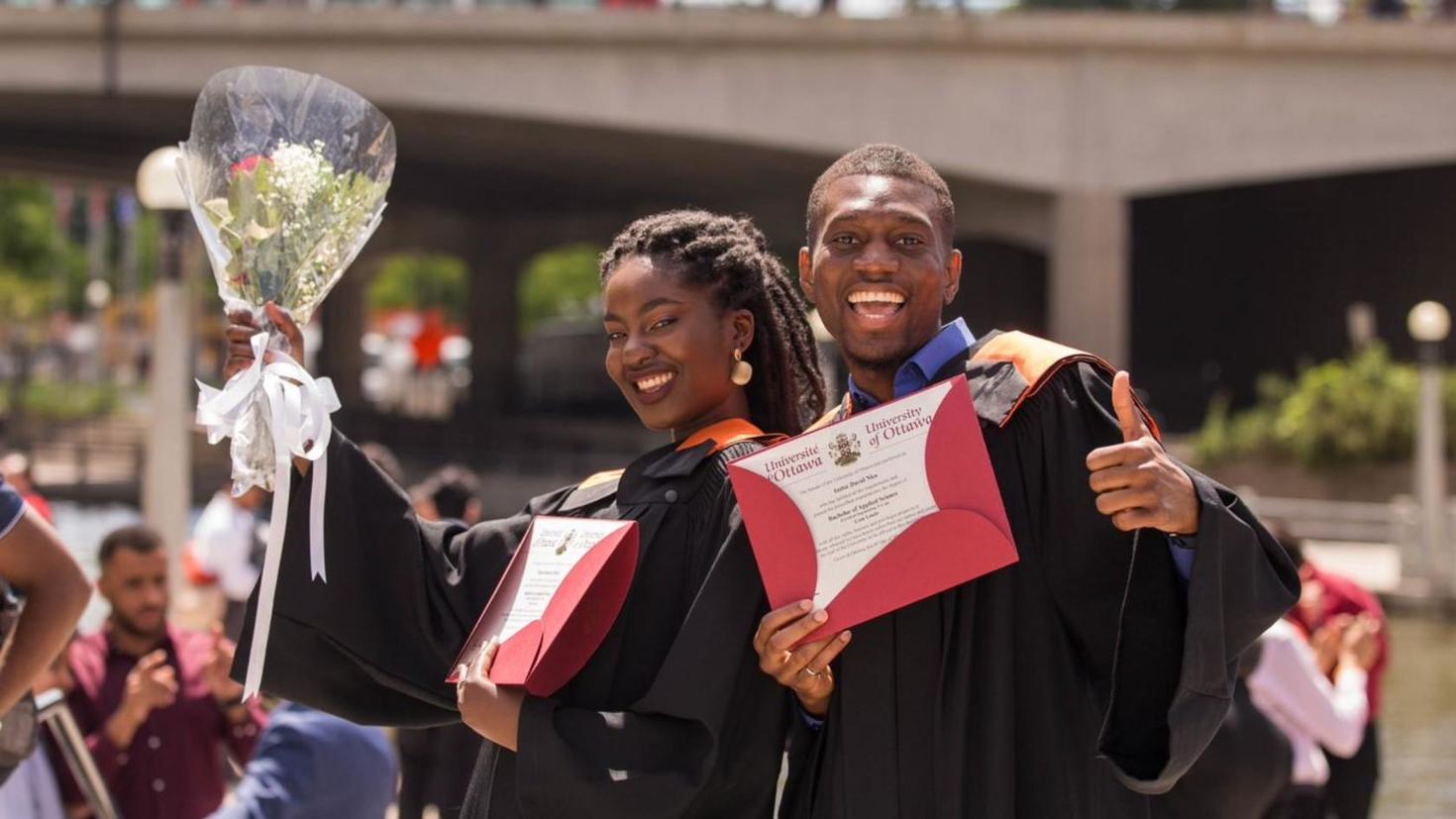 Two students showing off their university diplomas.