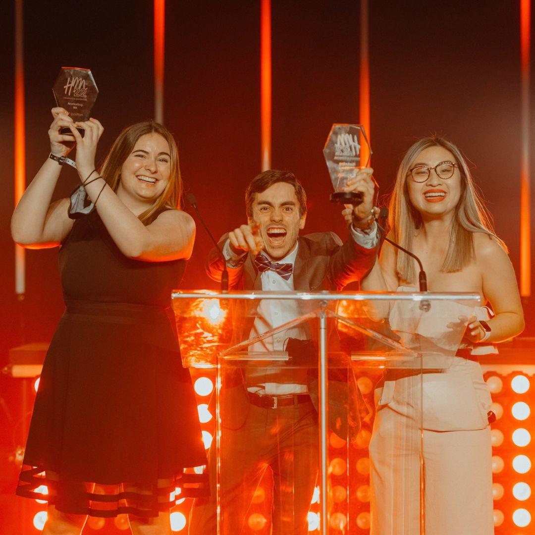 Liz Tran and her team on stage celebrating victory with trophies in hand.