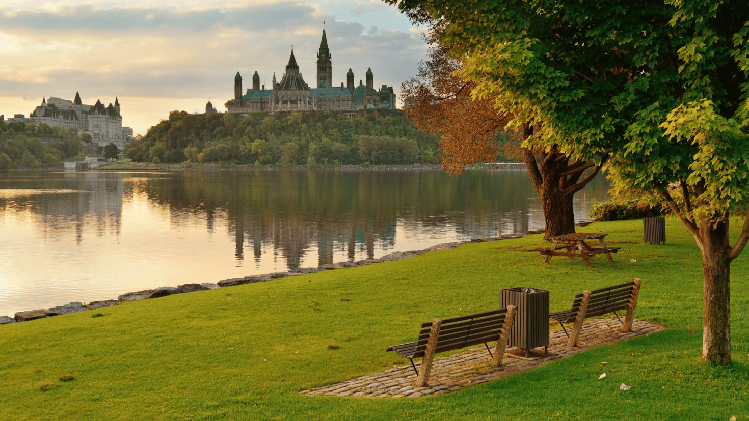 green grass, park benches with parliament of Canada buildings across river in background