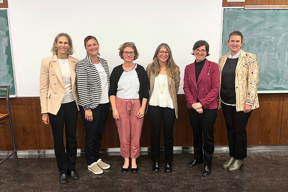 un groupe de femmes pose, debout en ligne à l'avant de la classe, avec un tableau noir et un écran de projection à l'arrière-plan. 