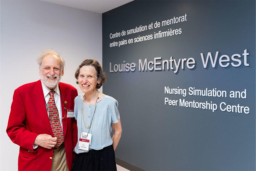 Louise McEntyre West's brother, John McEntyre, and sister, Lynn McEntyre Comerford, standing in front of the Louise McEntyre West Nursing Simulation and Peer Mentorship Centre. 