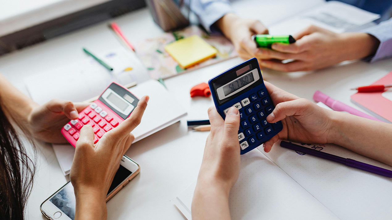 Trois étudiants sont assis autour d'une table en utilisent des calculatrices.