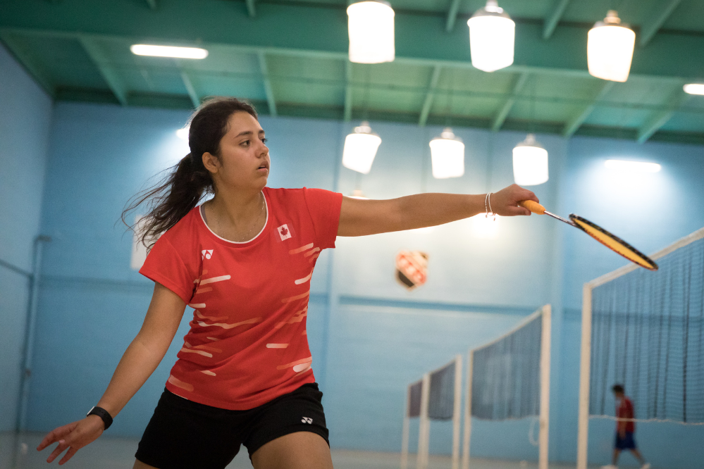 A woman swings a badminton bat. There are practice courts in the background